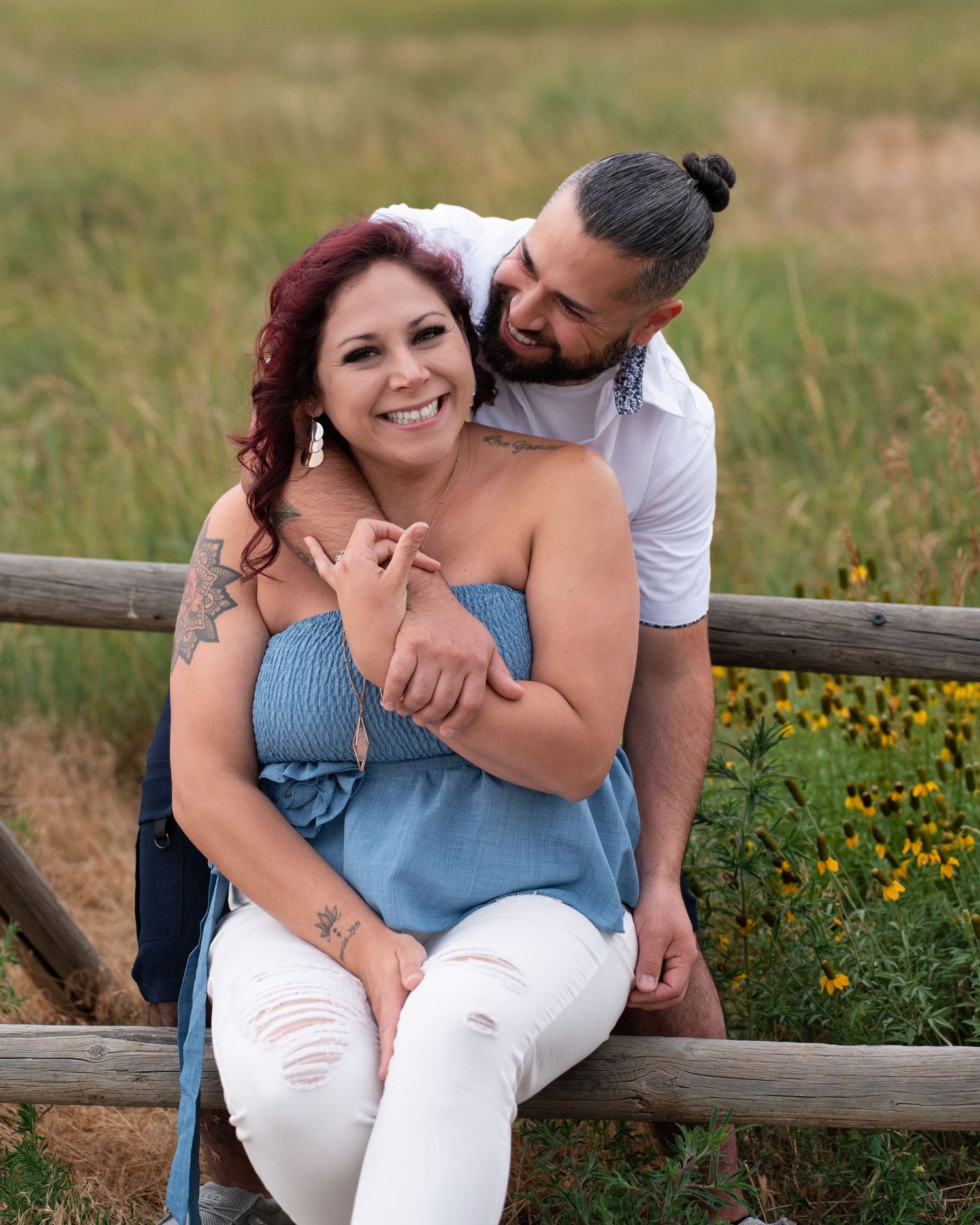 Couple embracing on wooden fence in summer field with wildflowers.