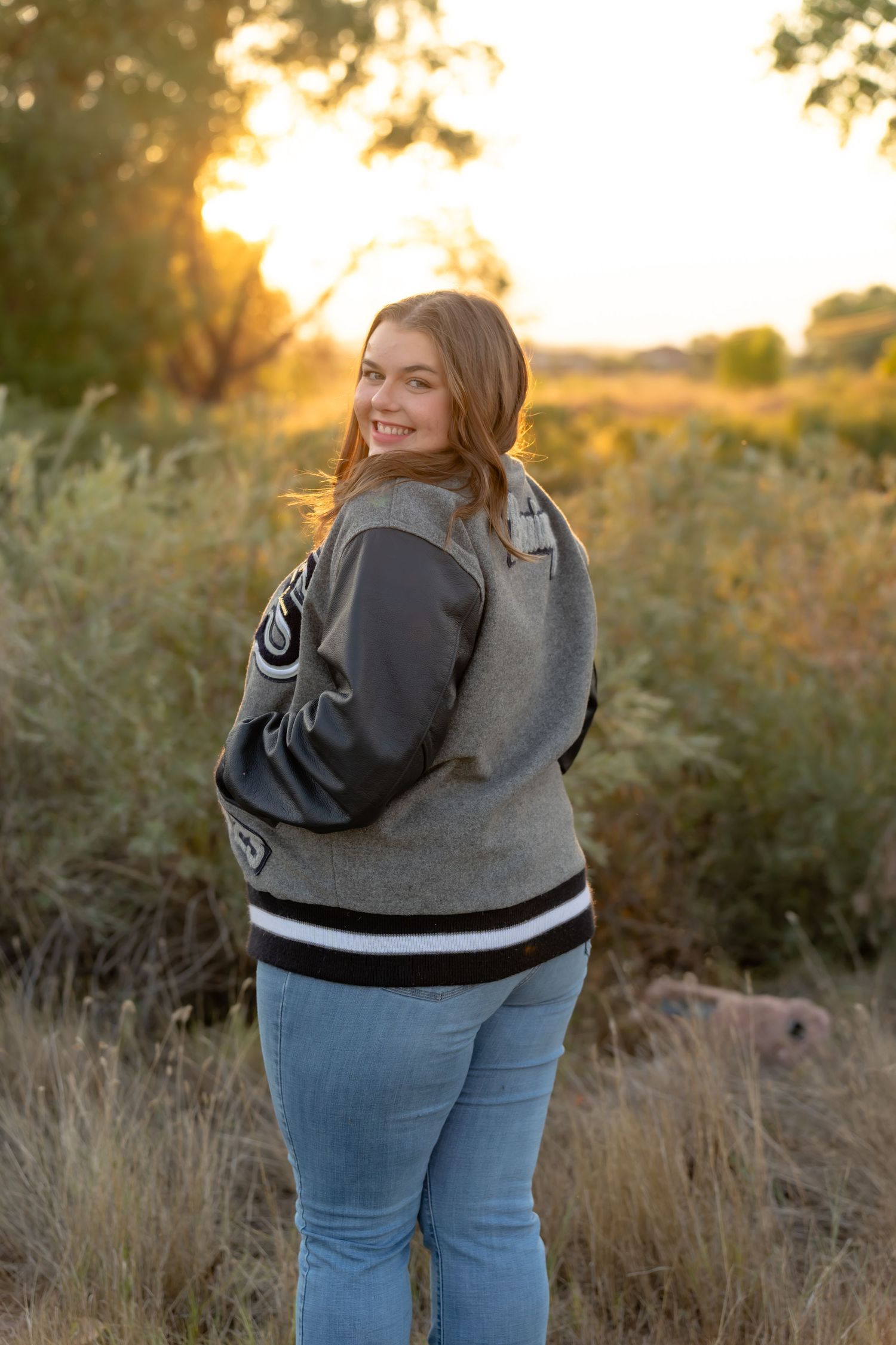 Person in denim and grey sweater poses against sunset backdrop in natural setting.