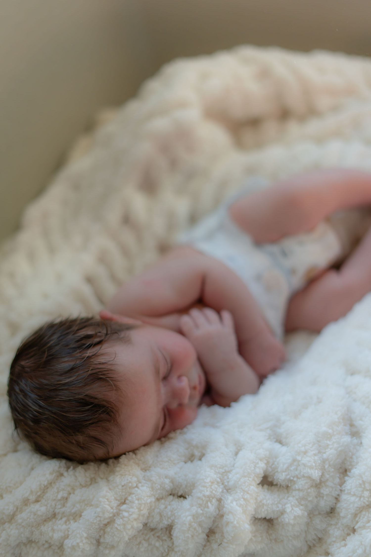A sleeping newborn baby lying on a soft white textured blanket.