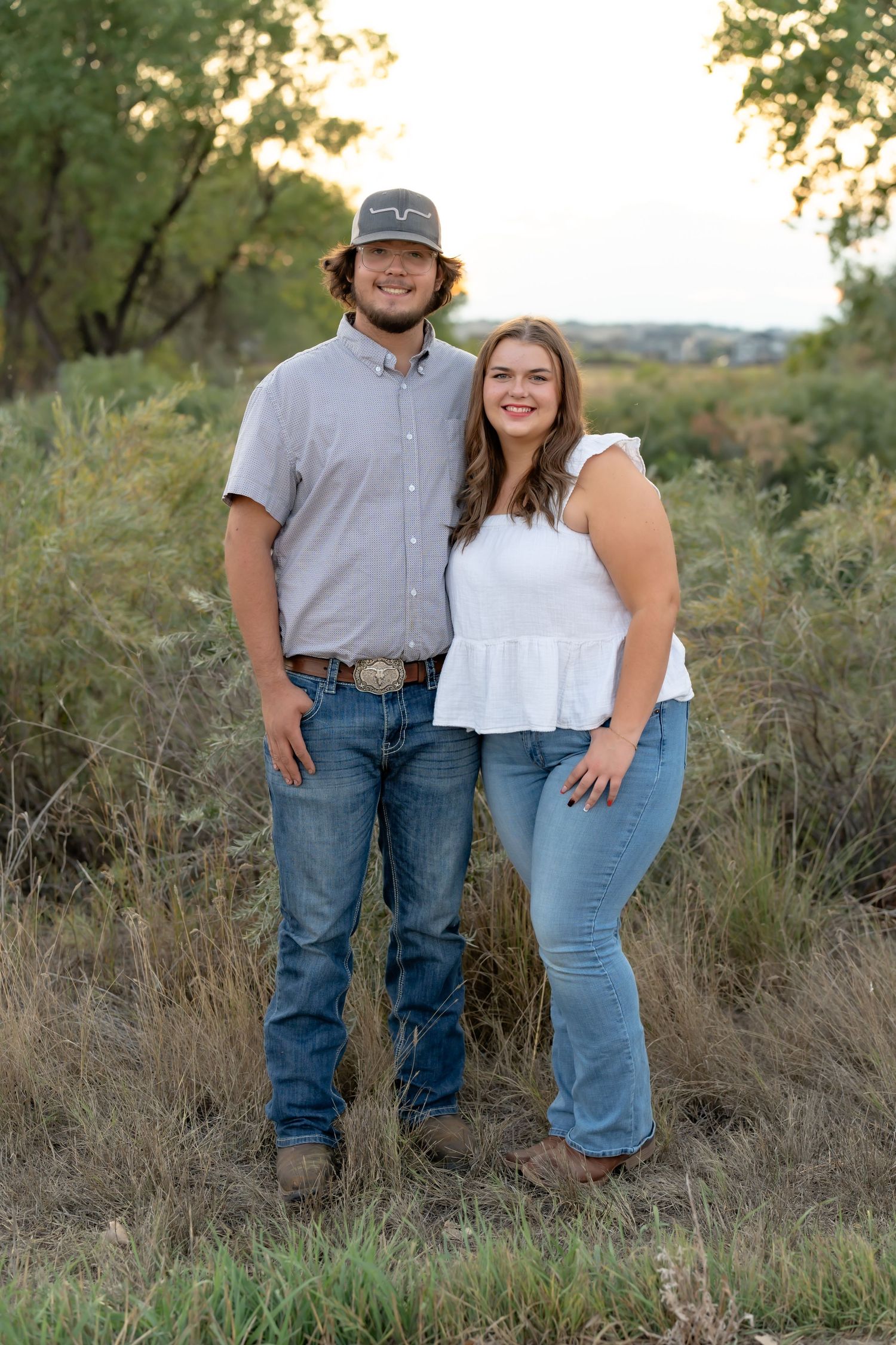 A couple stands together in a natural outdoor setting during golden hour.