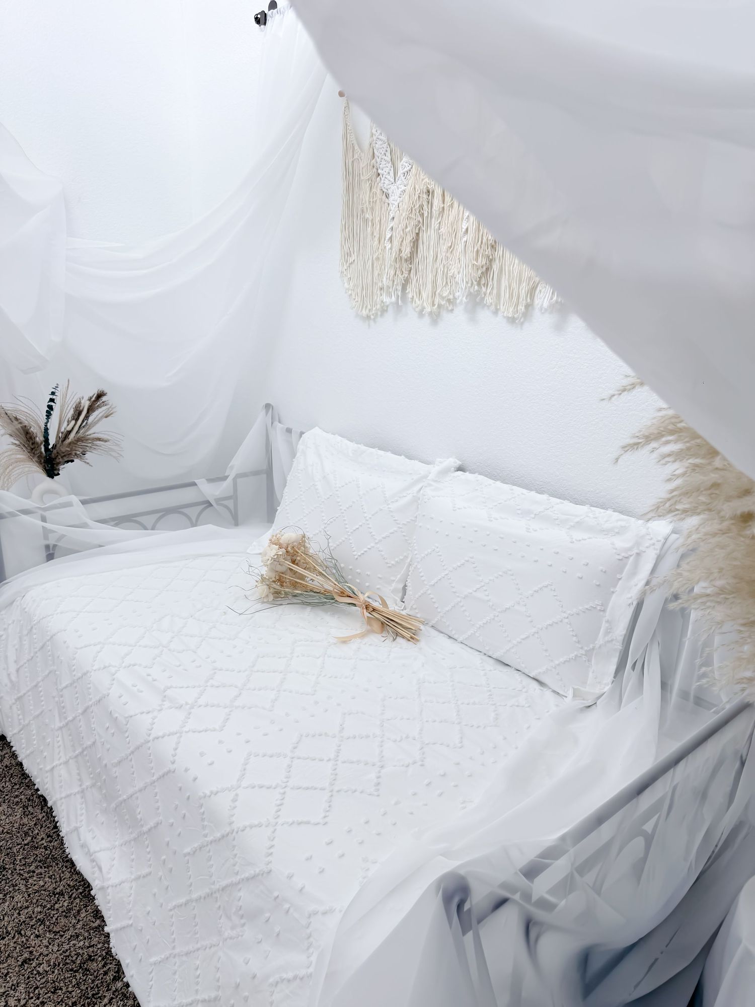 White bedding set with textured diamond pattern and pampas grass decor creates a serene, minimalist bedroom atmosphere.