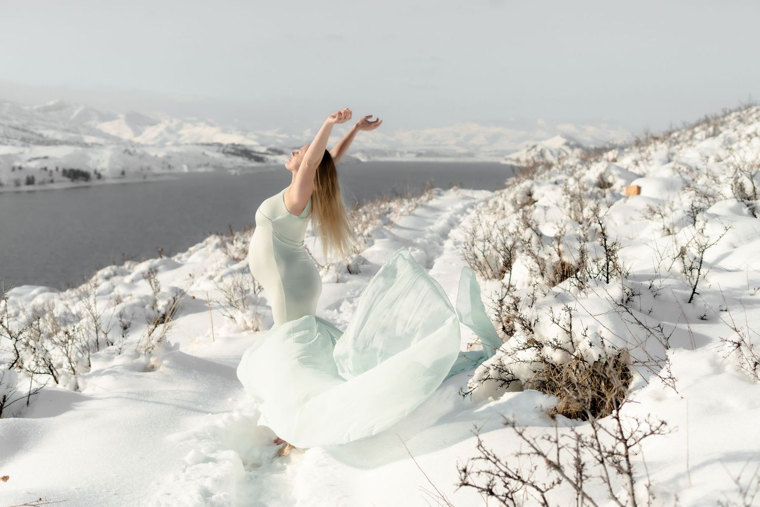 Flowing mint green dress contrasts against snowy mountain landscape as figure poses gracefully.