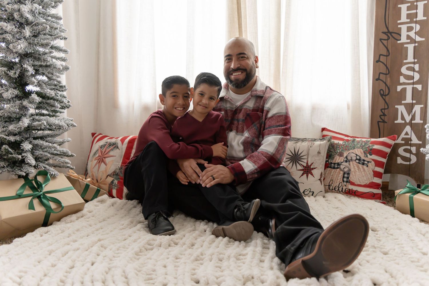 A family enjoys a cozy moment together on the floor during the holiday season with Christmas decorations visible.