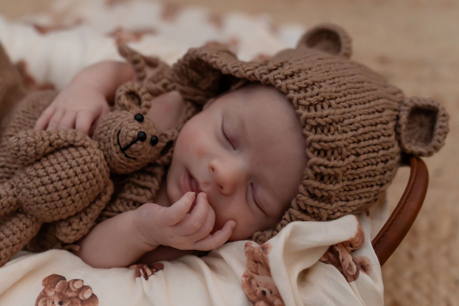 Newborn baby sleeping peacefully in brown knit wrap during professional photo session.