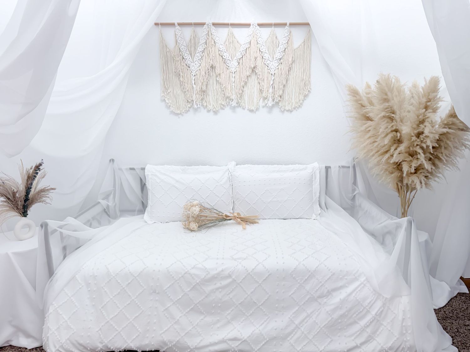 Cozy white bedding with fluffy pampas grass decor creates a serene and minimalist bedroom atmosphere.