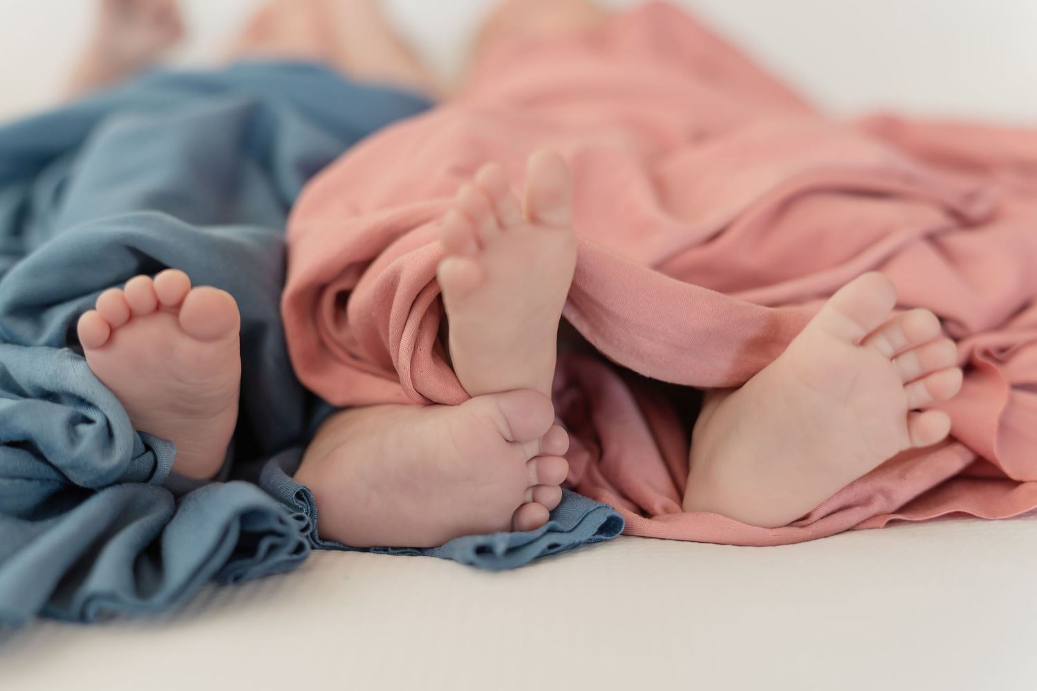 A collection of soft pink and blue baby clothes and blankets arranged in a row on a white background.