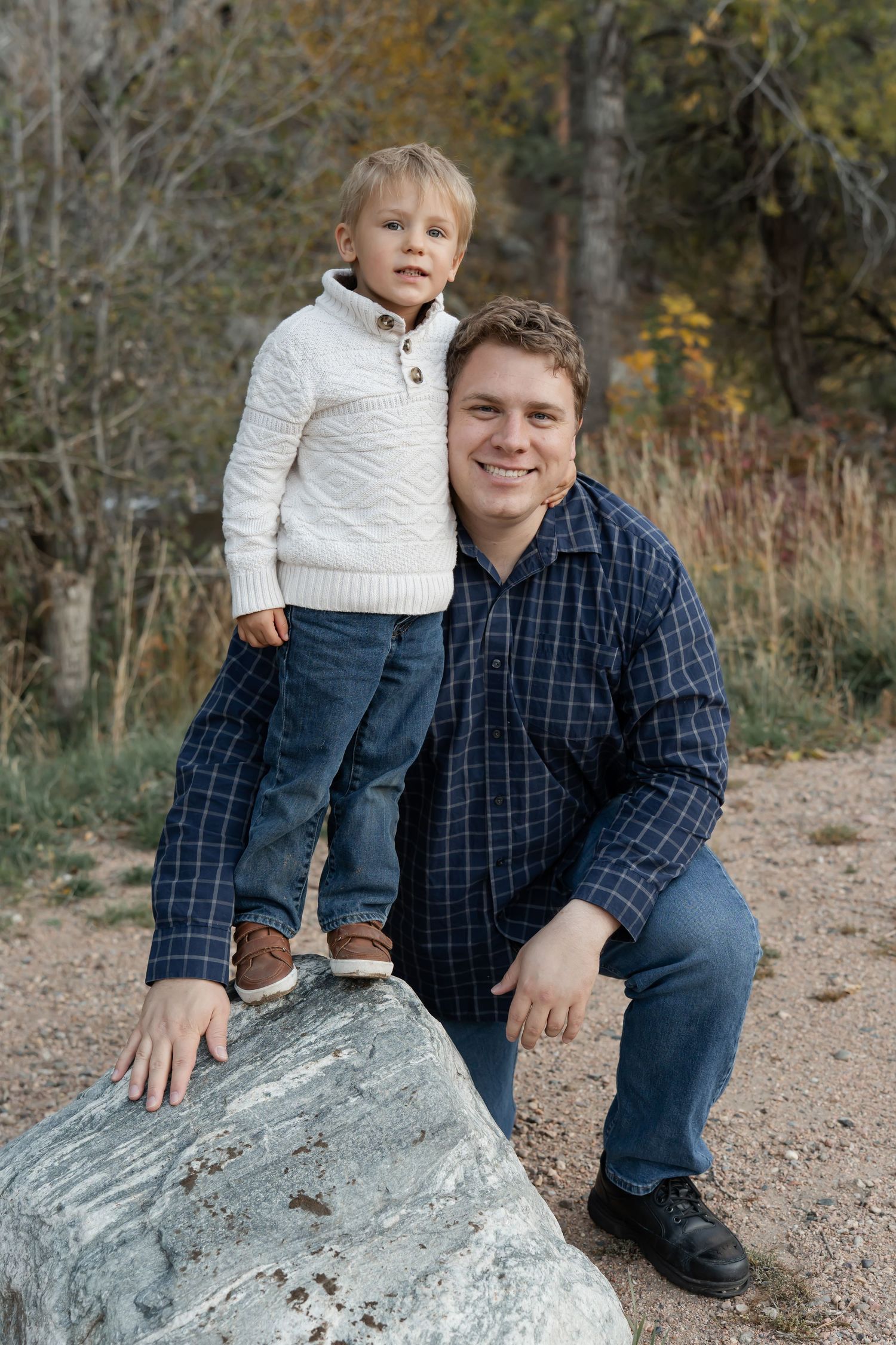 Outdoor portrait of a parent and child posing together on a large rock during autumn.