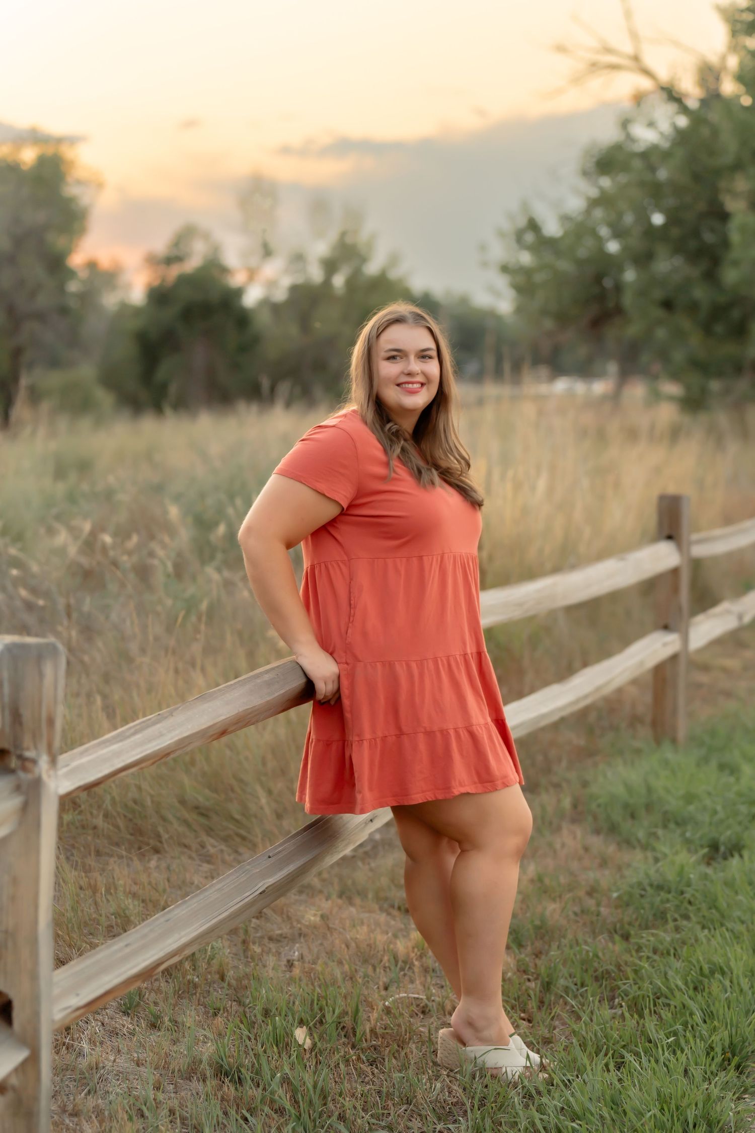 Senior photos by a wooden fence featuring a coral-colored top in a country setting.