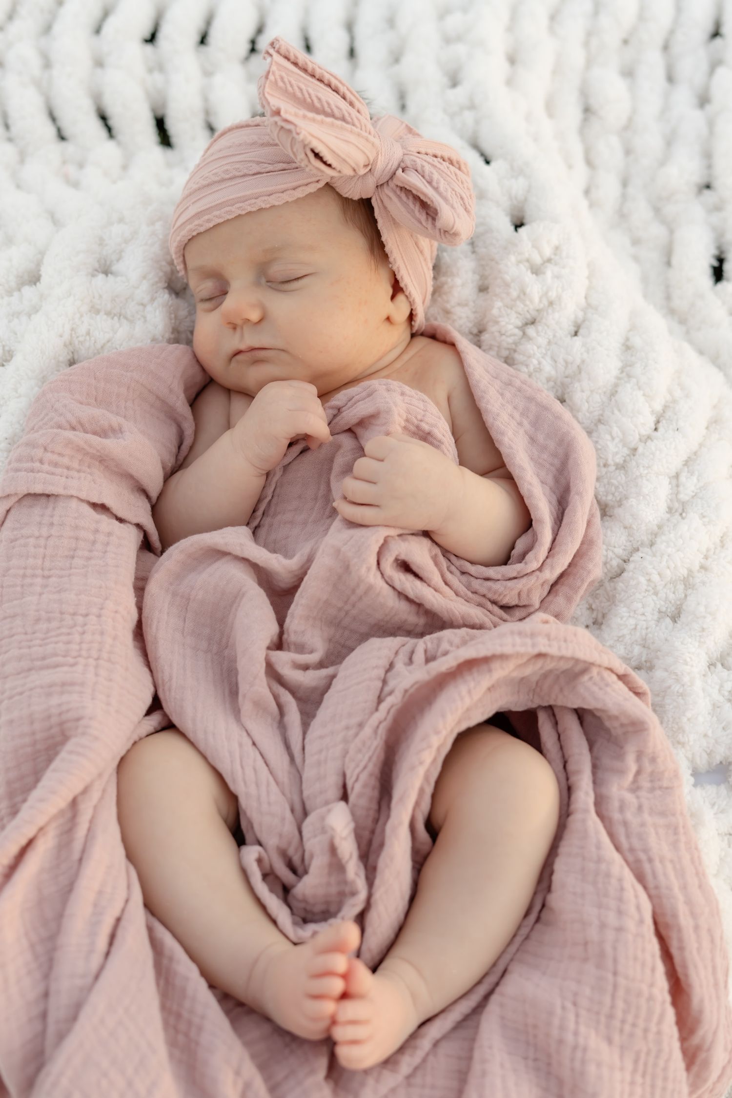 Baby sleeping peacefully in pink muslin wrap with matching bow headband.