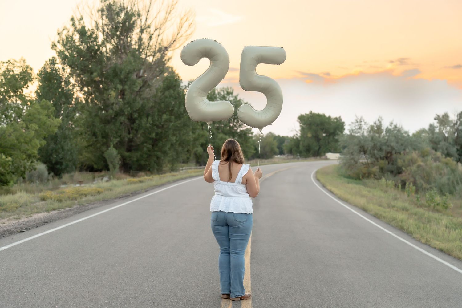 Person holding number 25 balloons on empty road at sunset.