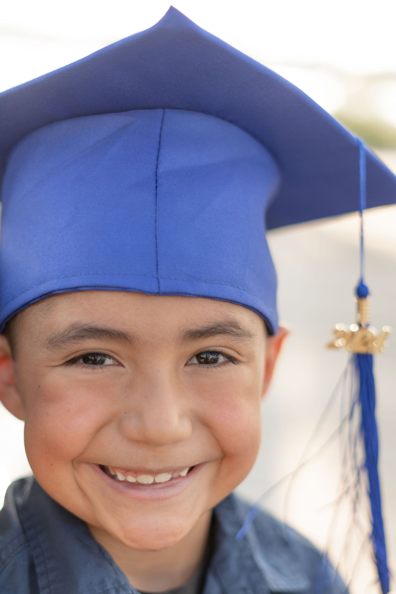 A portrait in a bright blue graduation cap showing a cheerful smile.