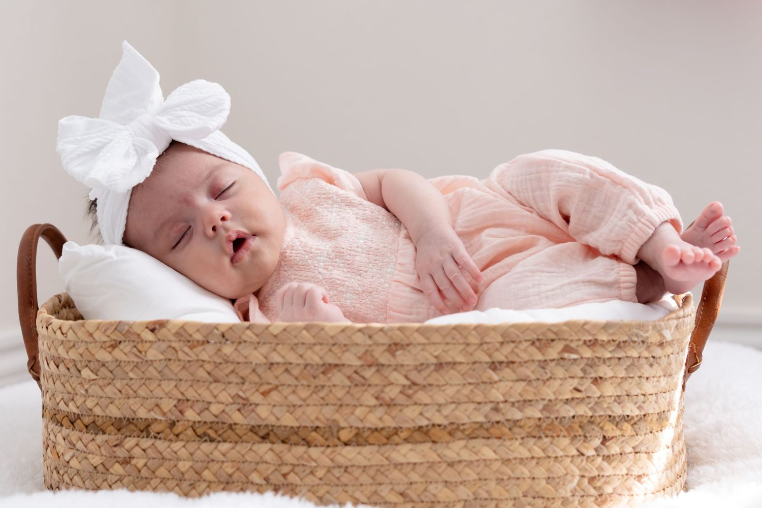 Newborn baby sleeping peacefully in a woven basket with soft pink blanket.