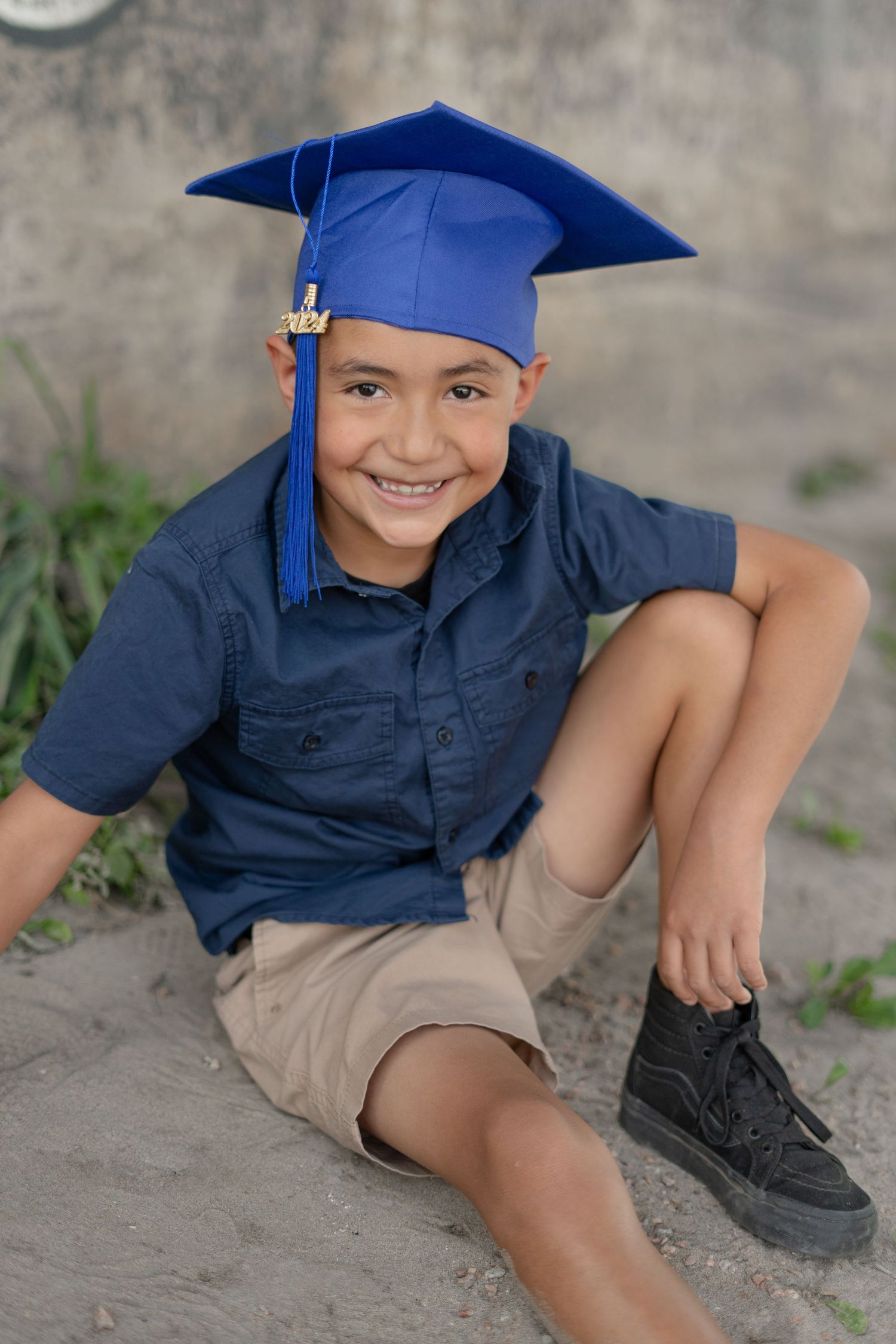 Playful portraits of a young graduate in blue cap and khaki shorts sitting on concrete.