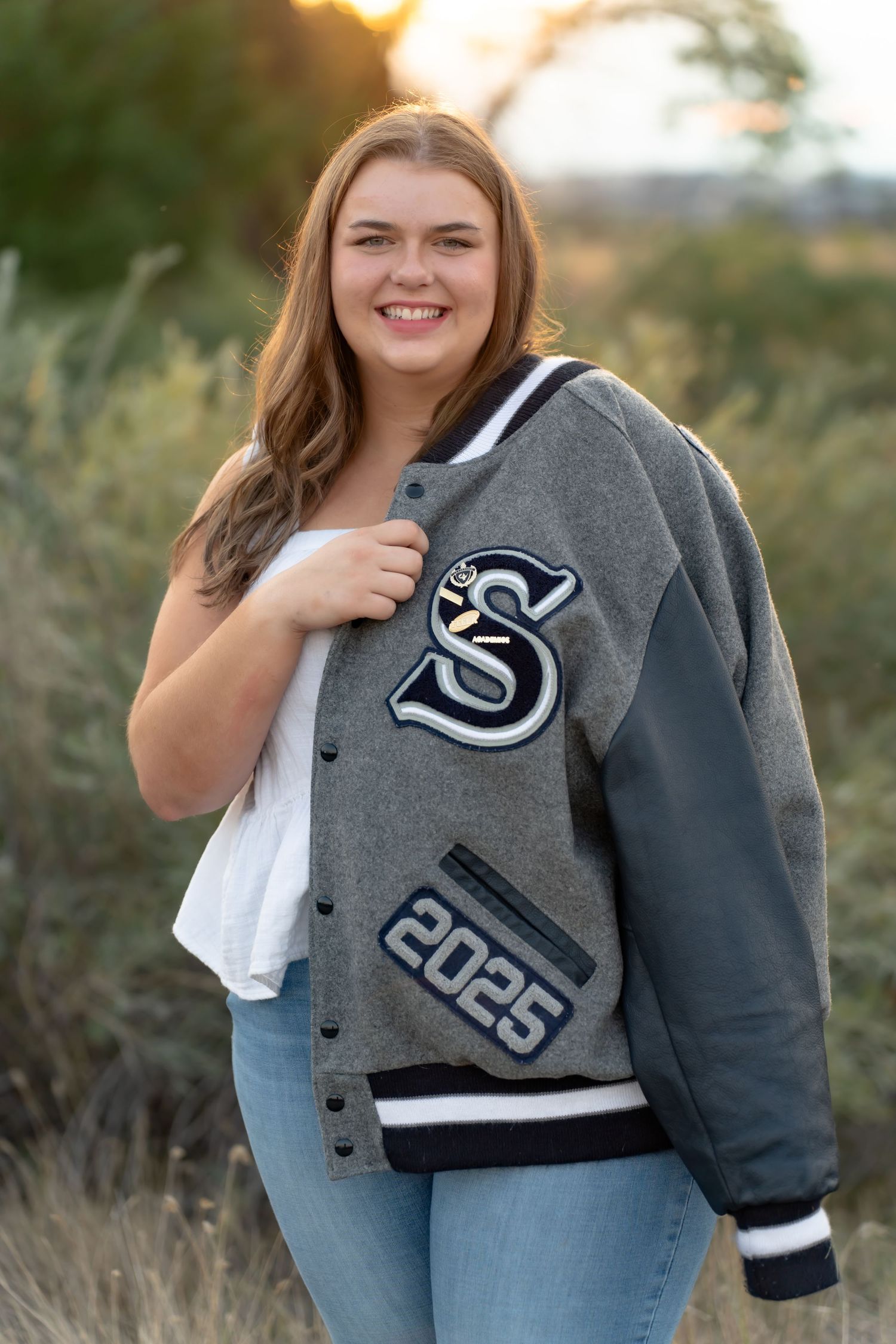 Outdoor senior portraits featuring a gray and navy varsity letterman jacket against natural scenery.