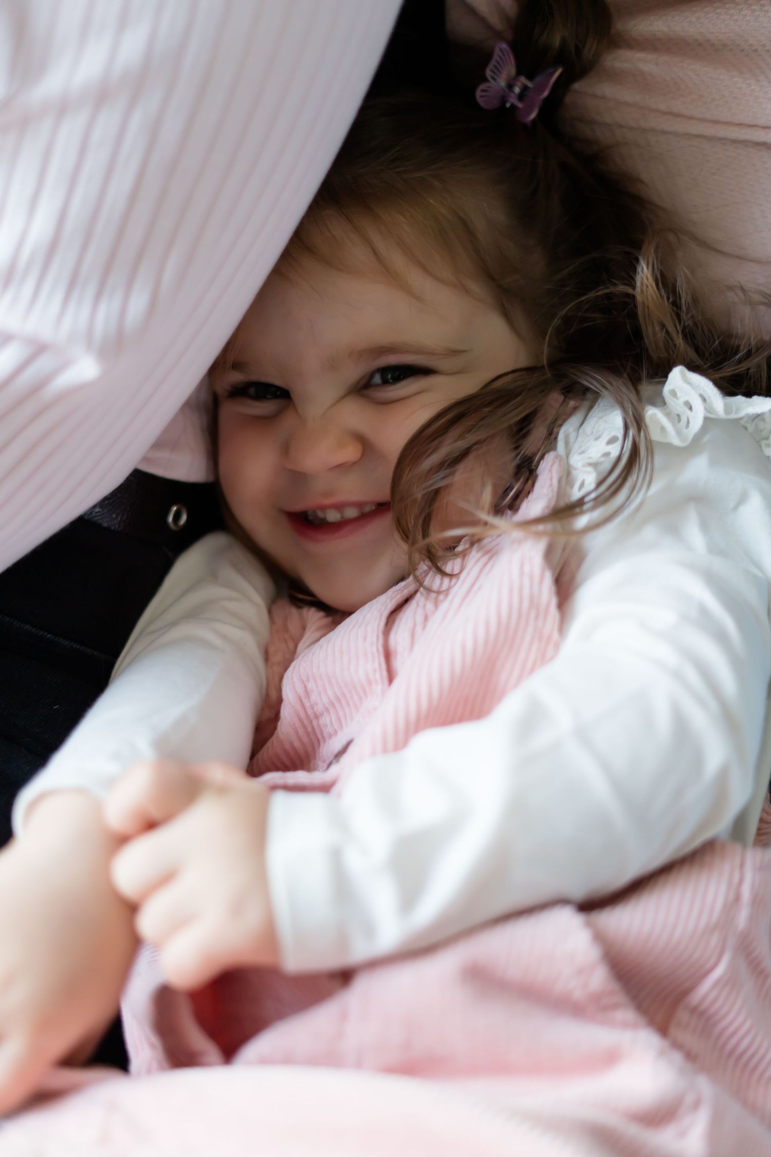 Child snuggling in soft pink and white bedding with playful expressions.