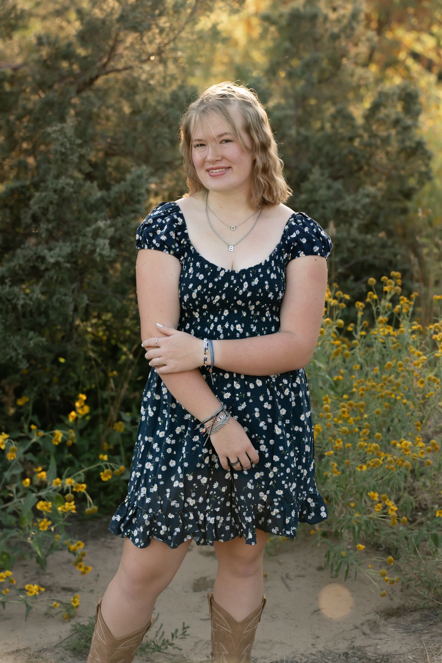 A person in a floral navy dress poses in front of yellow wildflowers during a golden hour photoshoot.