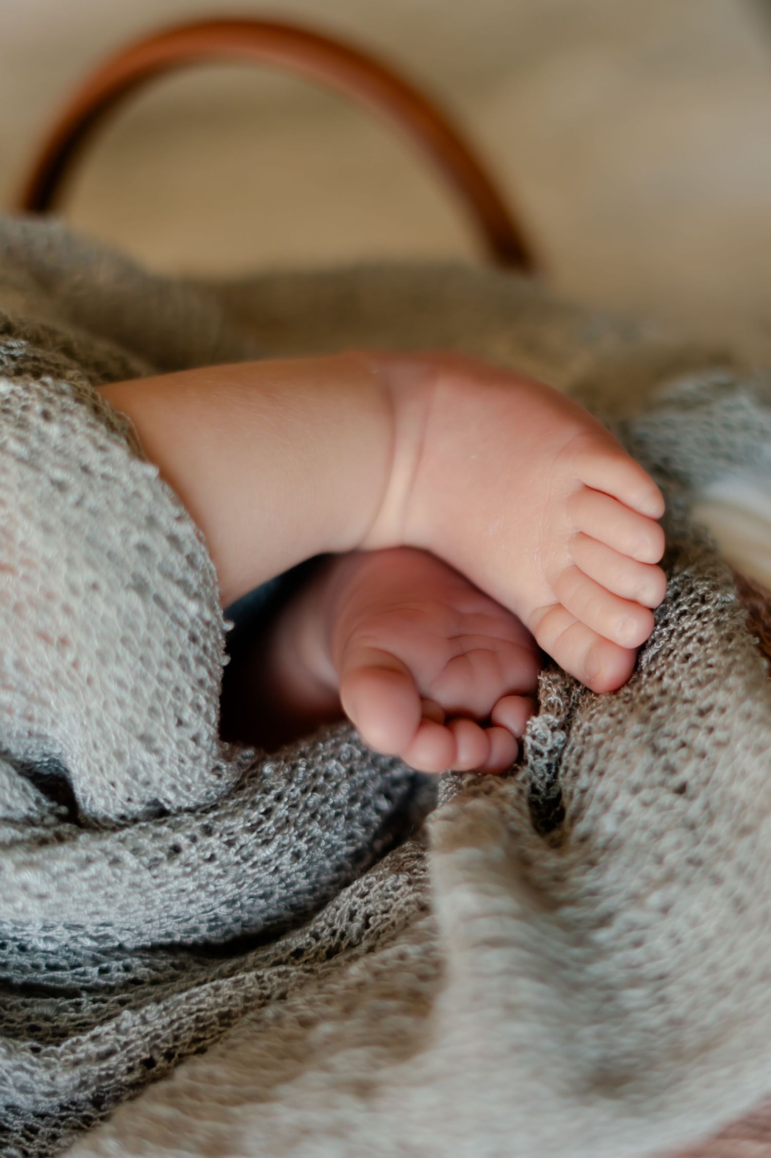 Close-up of tiny baby feet resting on gray knitted fabric.