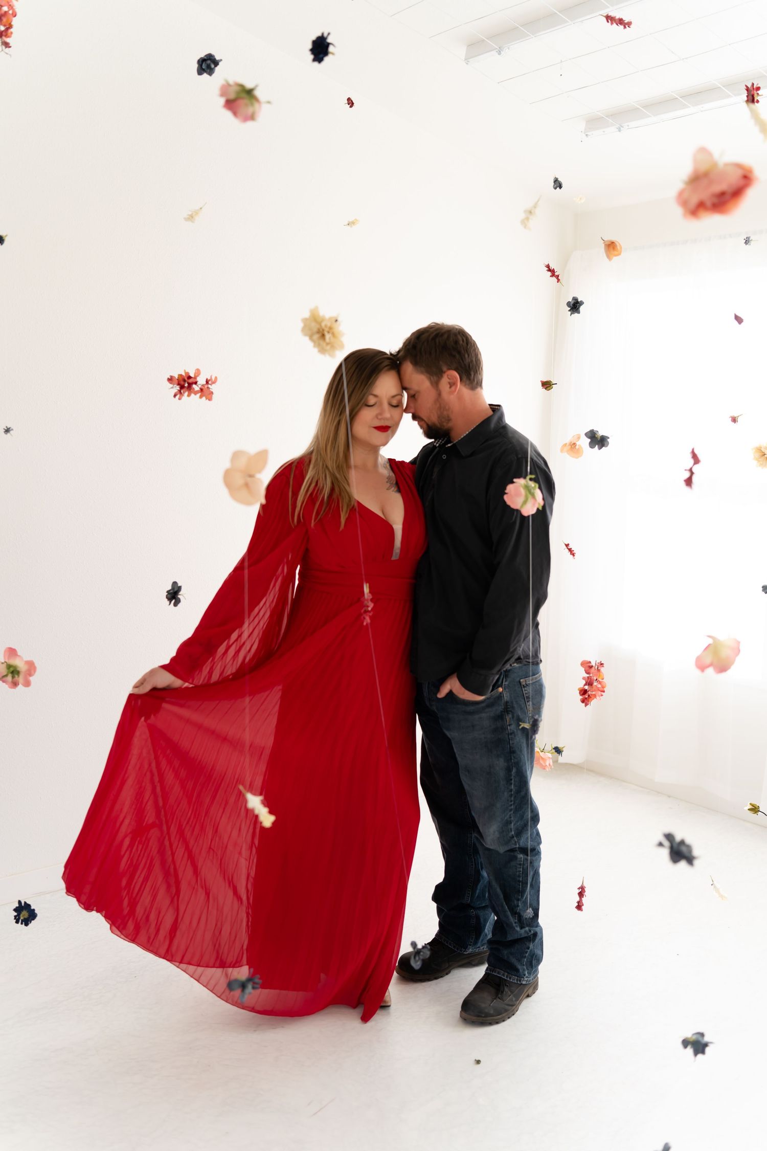 A couple in red and black attire poses playfully against a white backdrop with floating confetti.