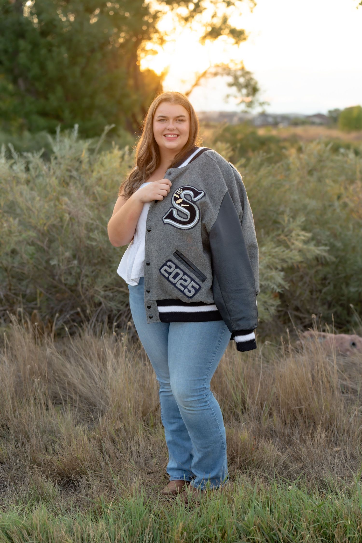 An outdoor portrait at sunset wearing a varsity letter jacket and jeans.