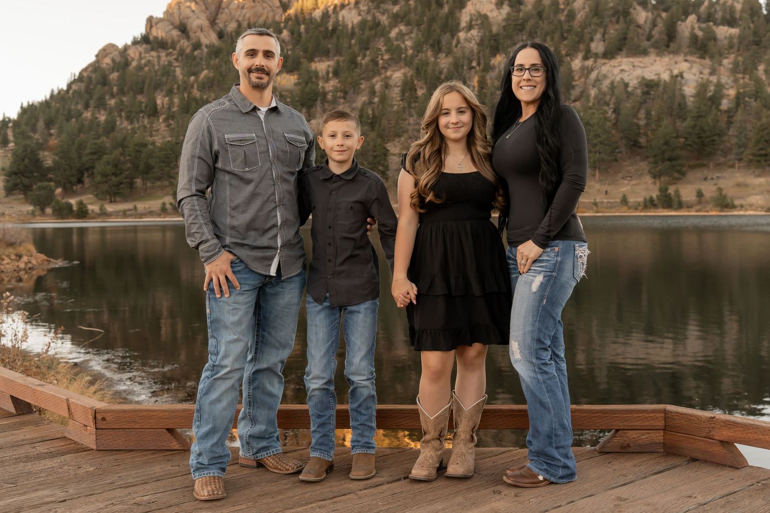 A family poses together for outdoor portraits by a serene lake with mountain backdrop in autumn weather.