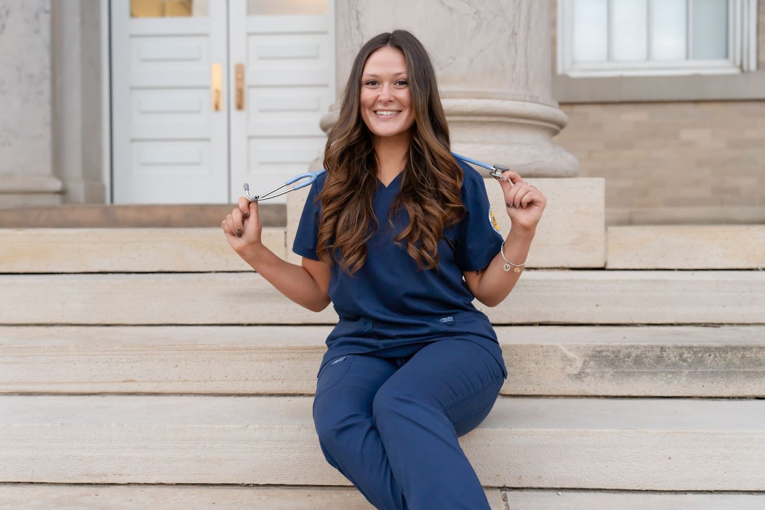 Person in navy outfit sits casually on stone steps smiling at camera.