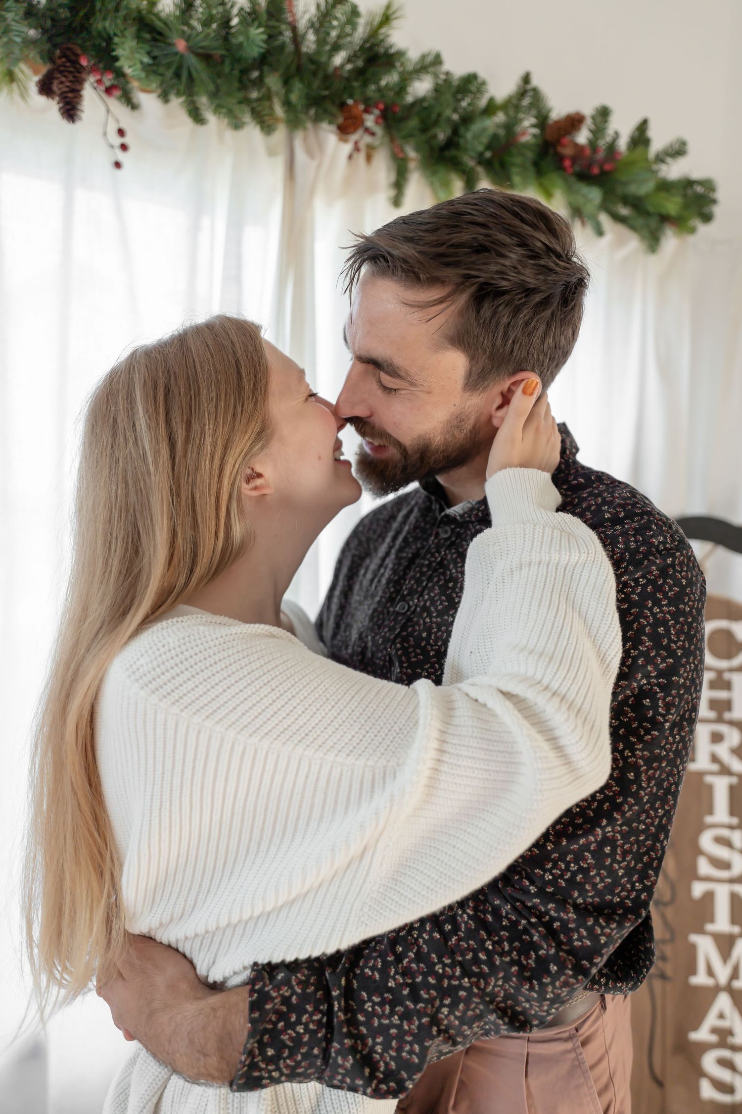 Couple in white and floral outfits share romantic moments under Christmas garland decorations.