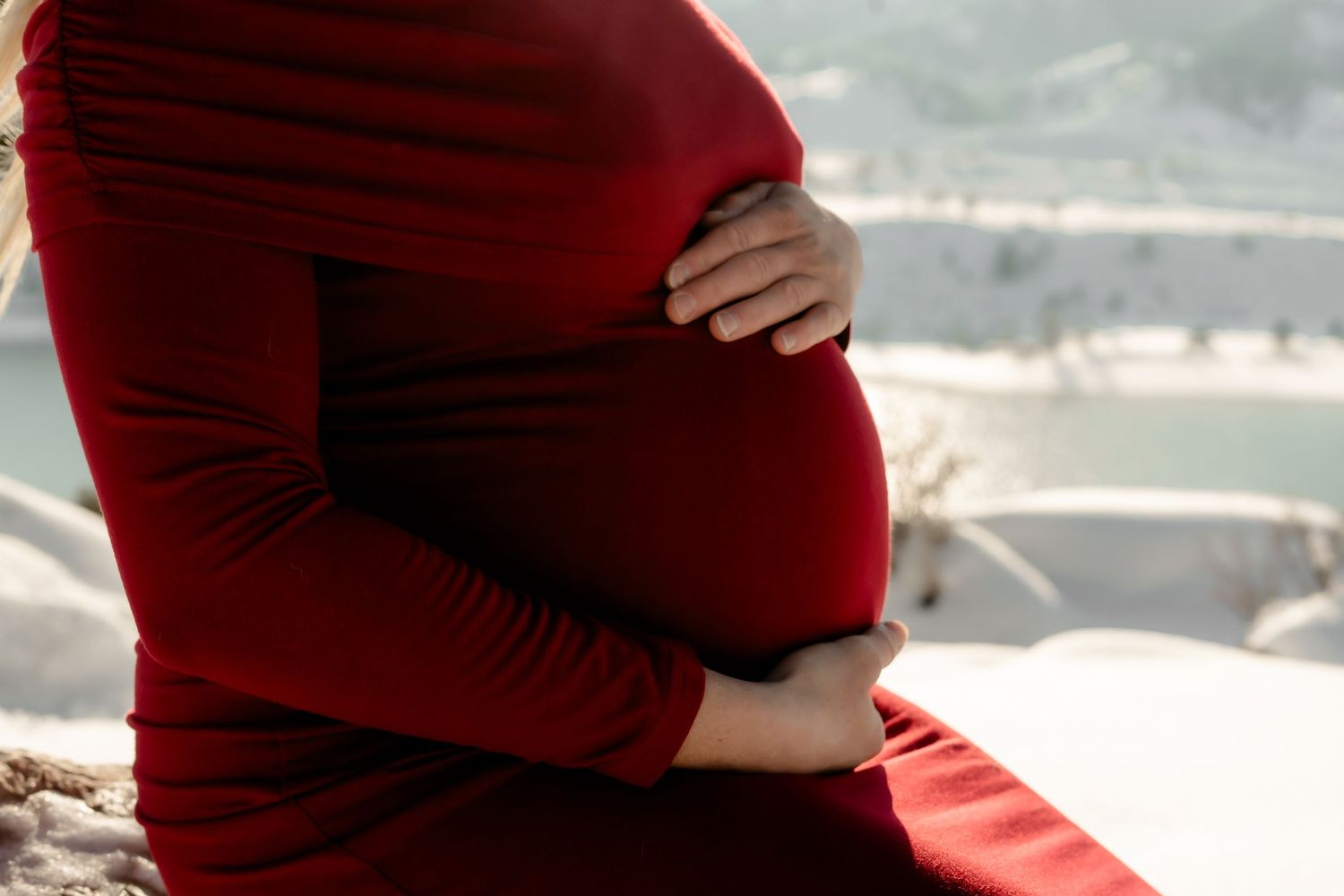 Elegant maternity photo with woman in red dress cradling baby bump.
