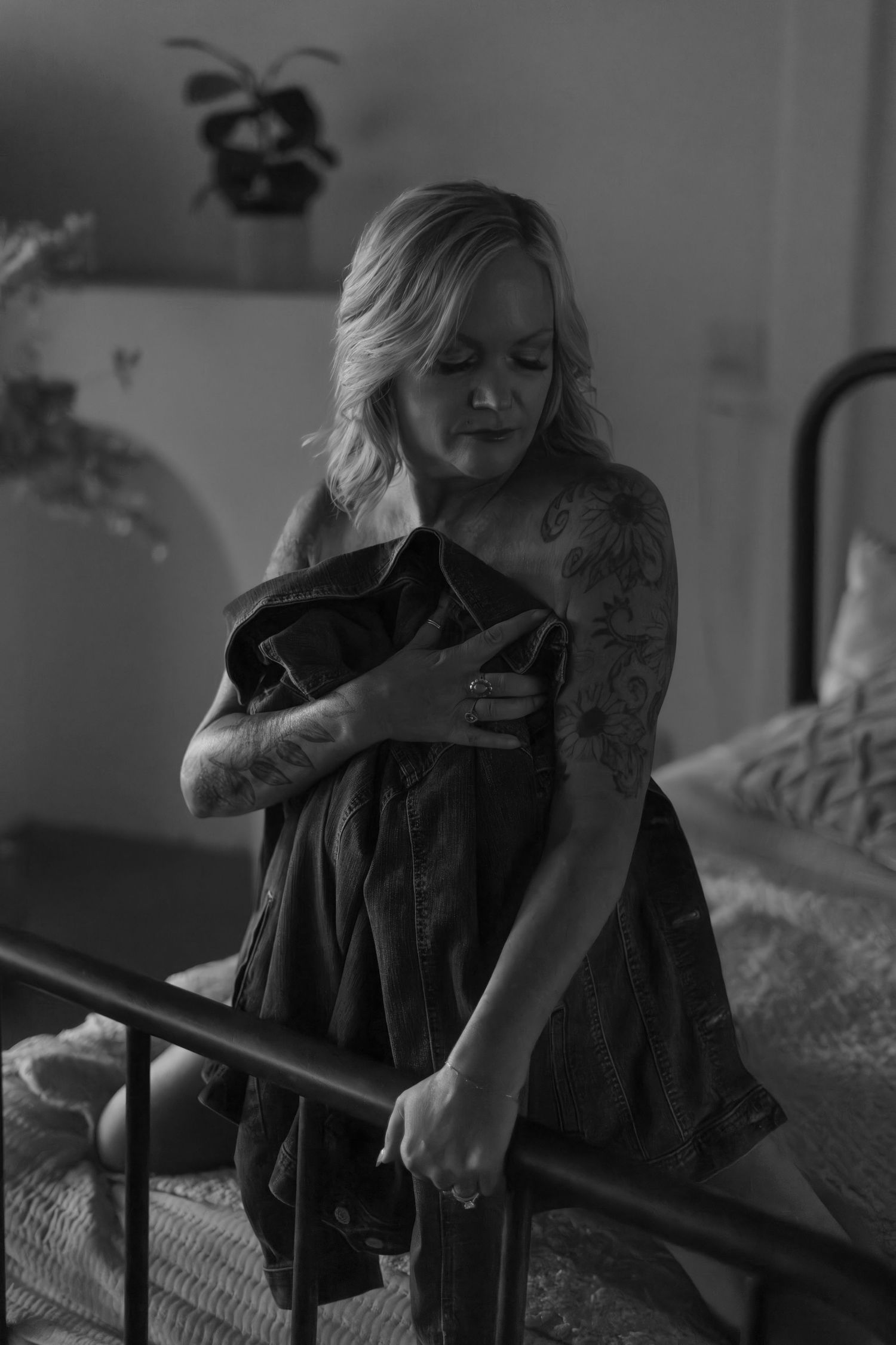 Black and white photo of someone in dark dress holding fabric near a bed.