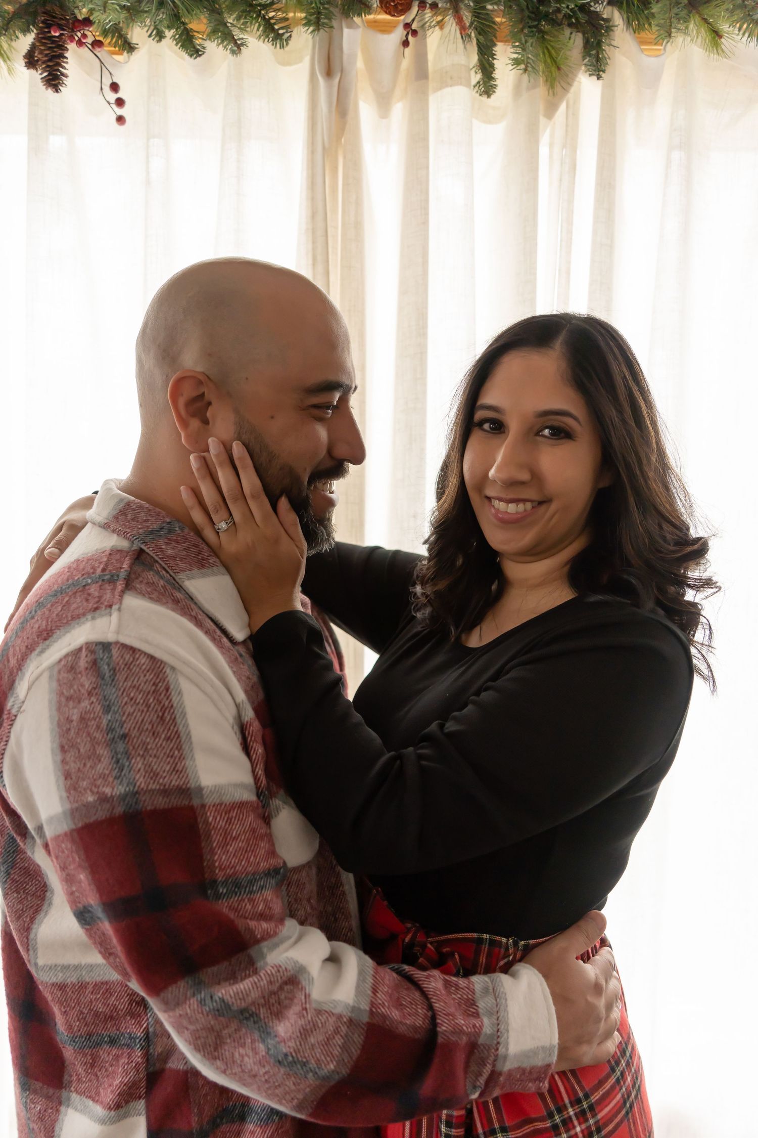 A couple embraces lovingly under Christmas garland decorations in a series of romantic holiday photos.