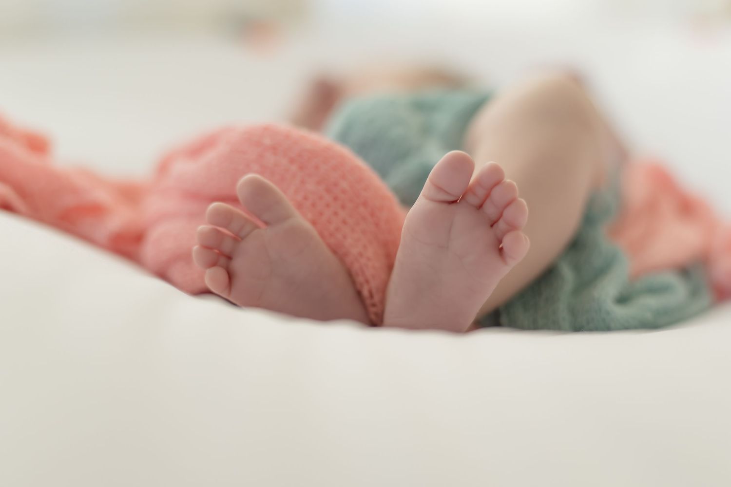 Close-up view of baby feet and hands with soft pink and teal blankets in the background.