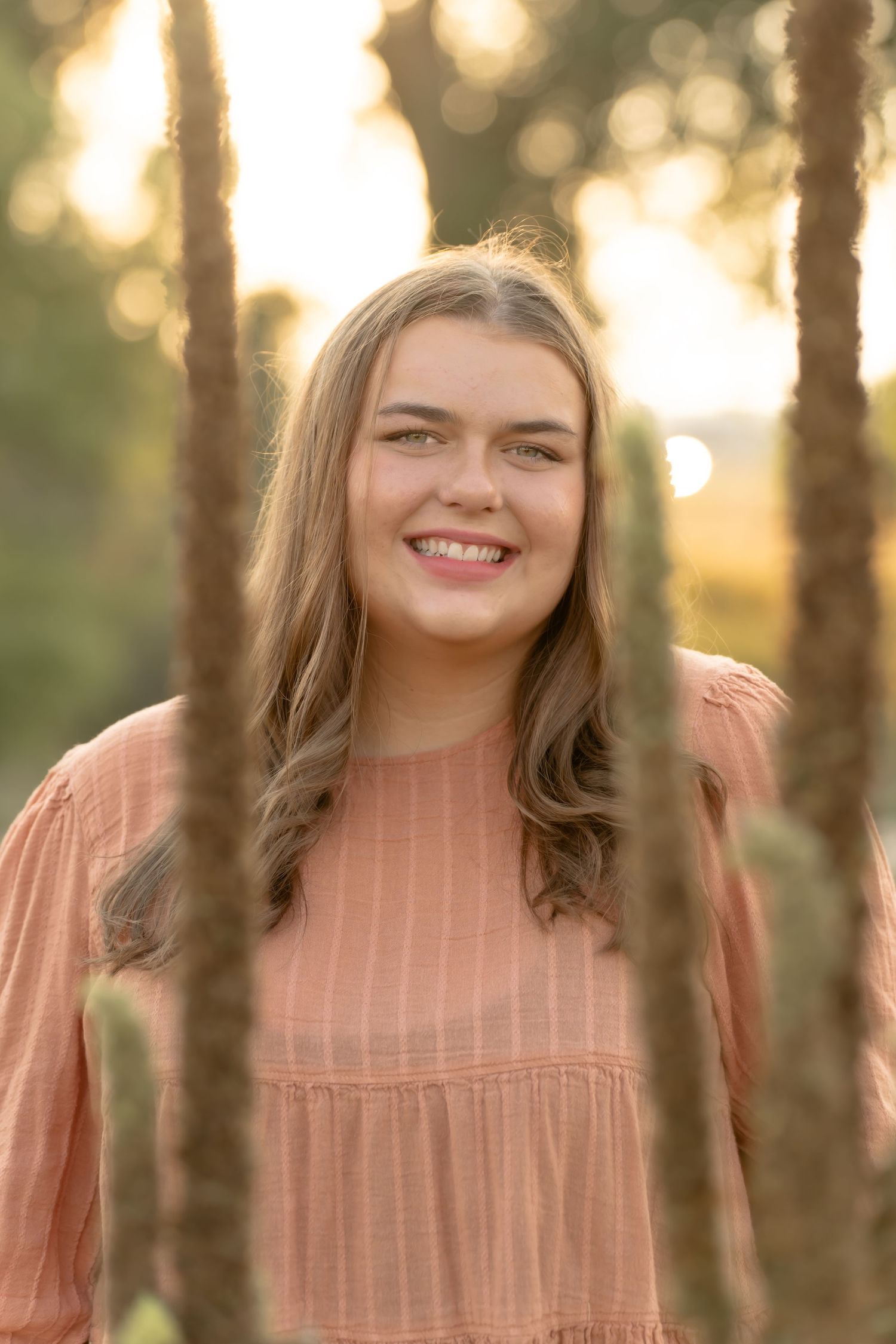 Portrait series in warm lighting among trees wearing peach-colored top.