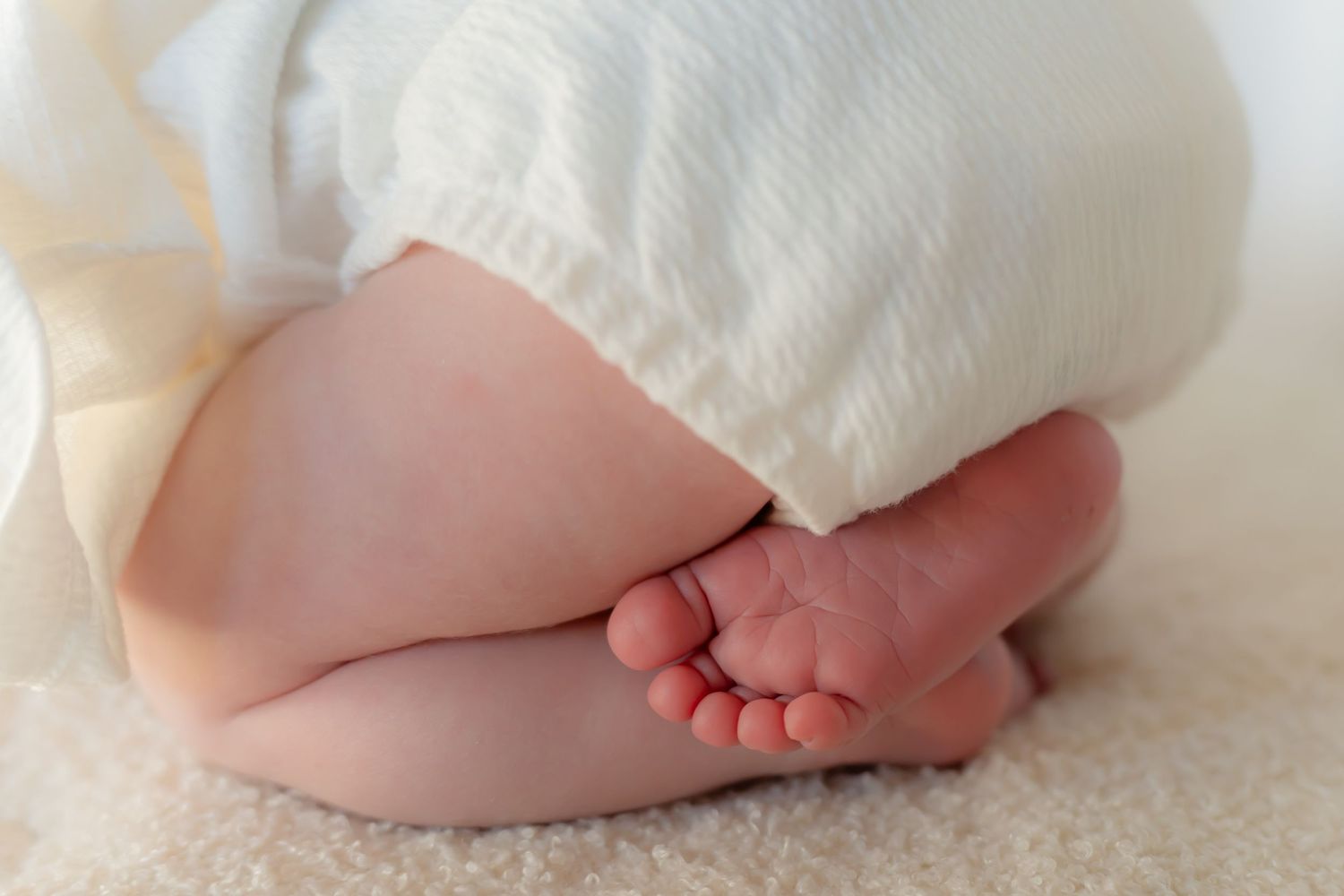 Close-up of baby feet and white dress against cream background.