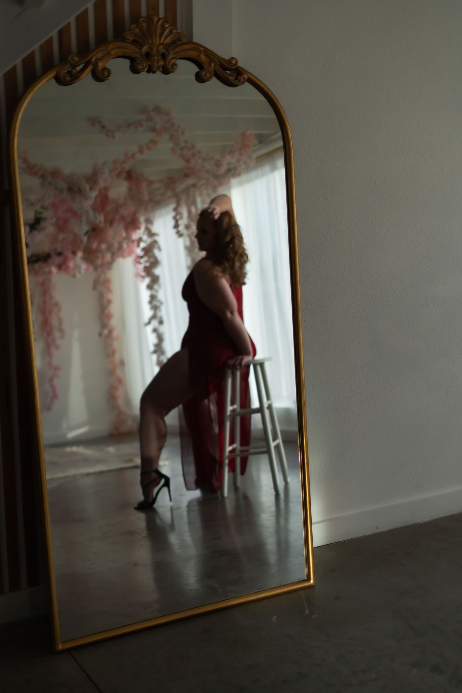 A sequence of mirror reflections shows a person in red sitting on a stool against a white wall with pink floral patterns.