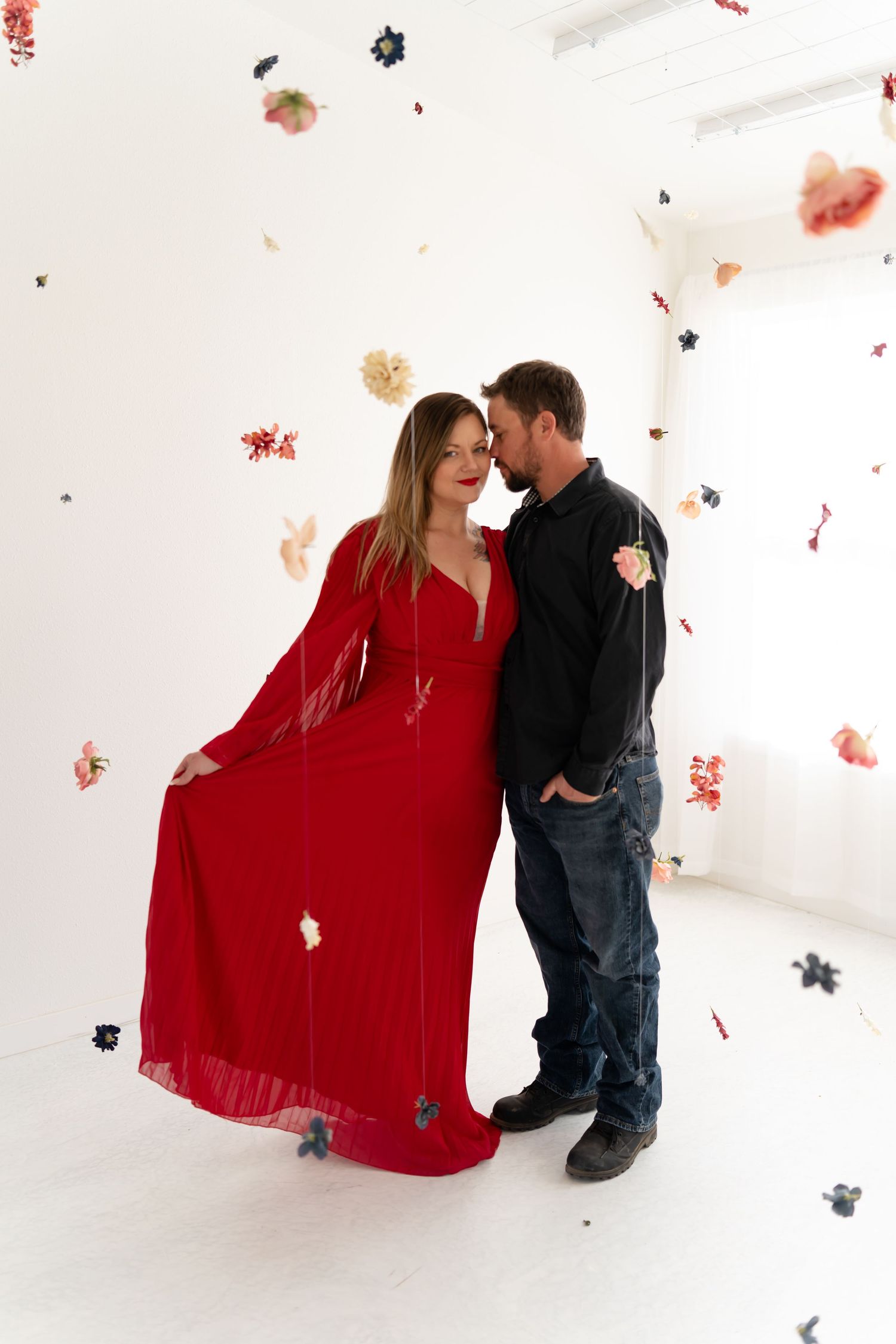 A couple shares a romantic moment against a white backdrop with scattered red and black confetti falling around them.