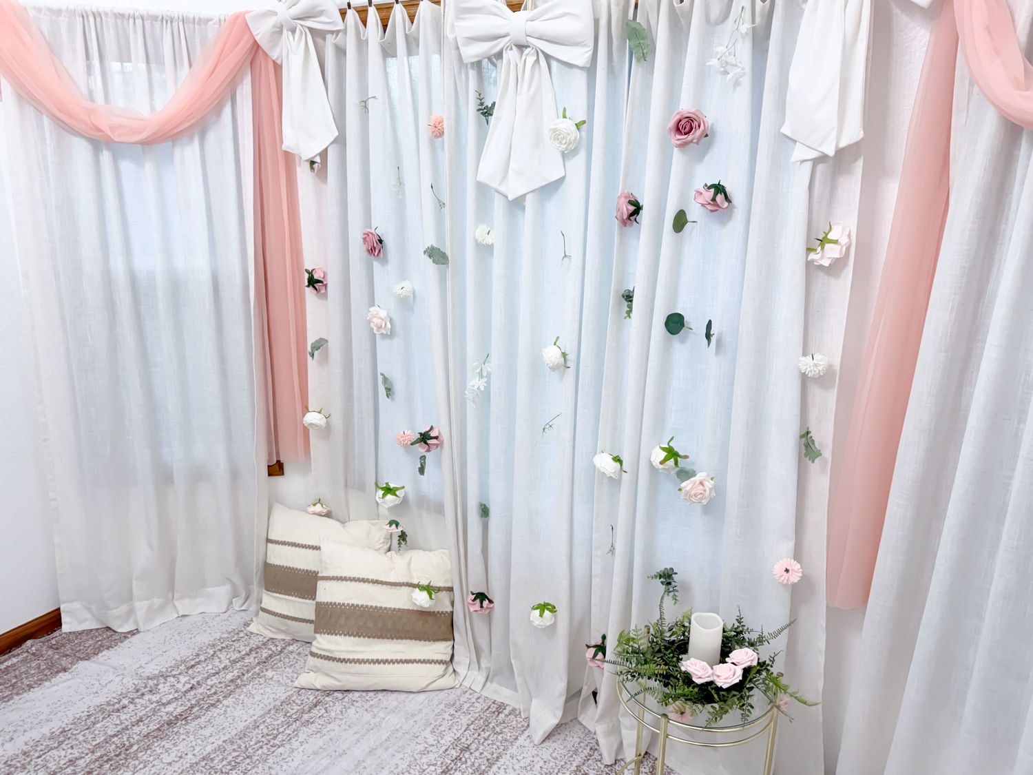 White curtain backdrop decorated with pink draping, scattered roses, and white bows for a romantic photo setting.