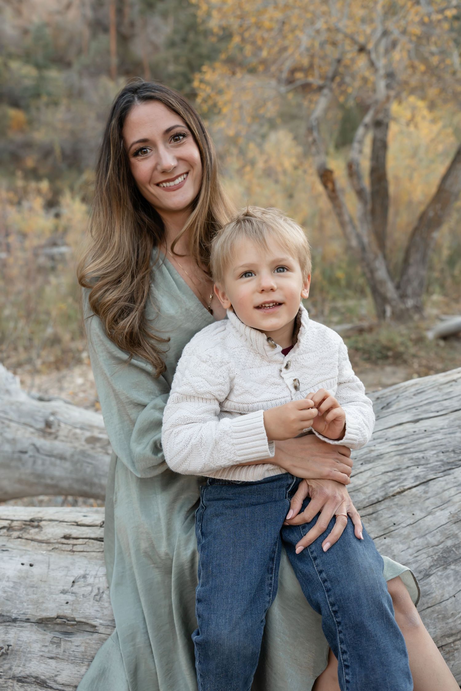 Parent and child share joyful moments together outdoors in autumn setting on fallen tree trunk.