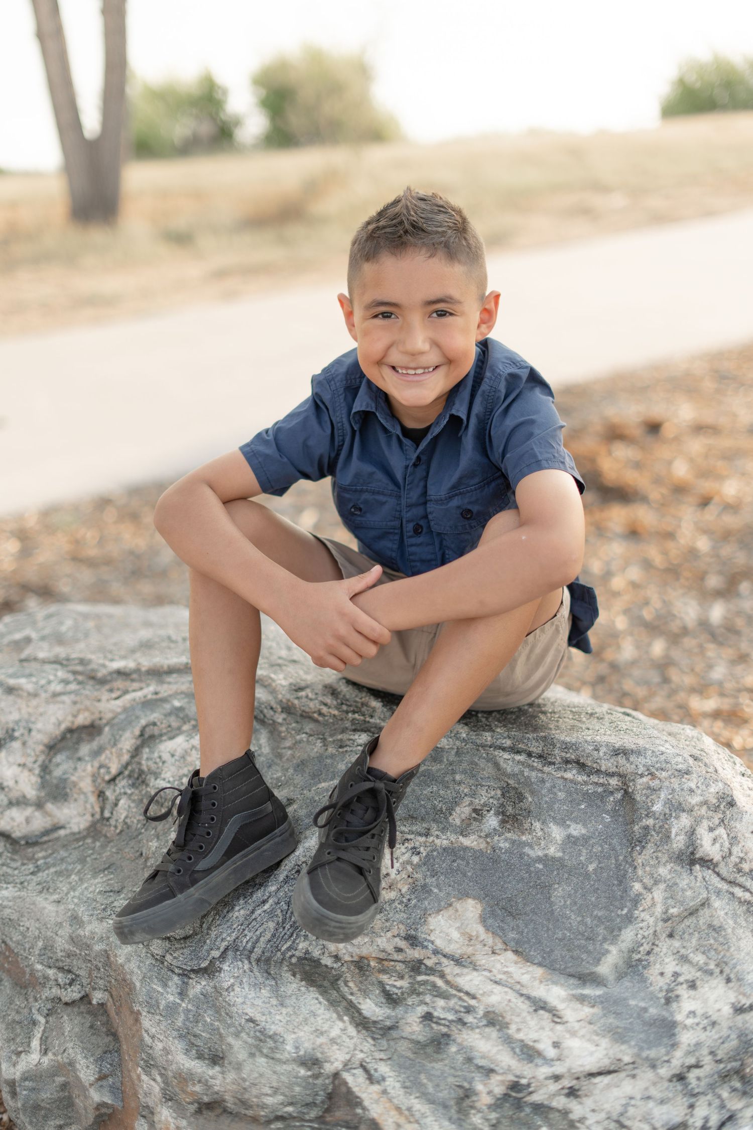 A young person in a navy shirt sits playfully on a large rock formation outdoors.