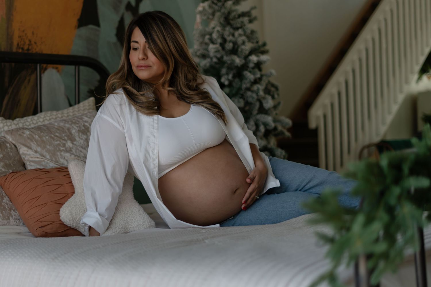Maternity boudoir photo with woman in white shirt relaxing on couch.