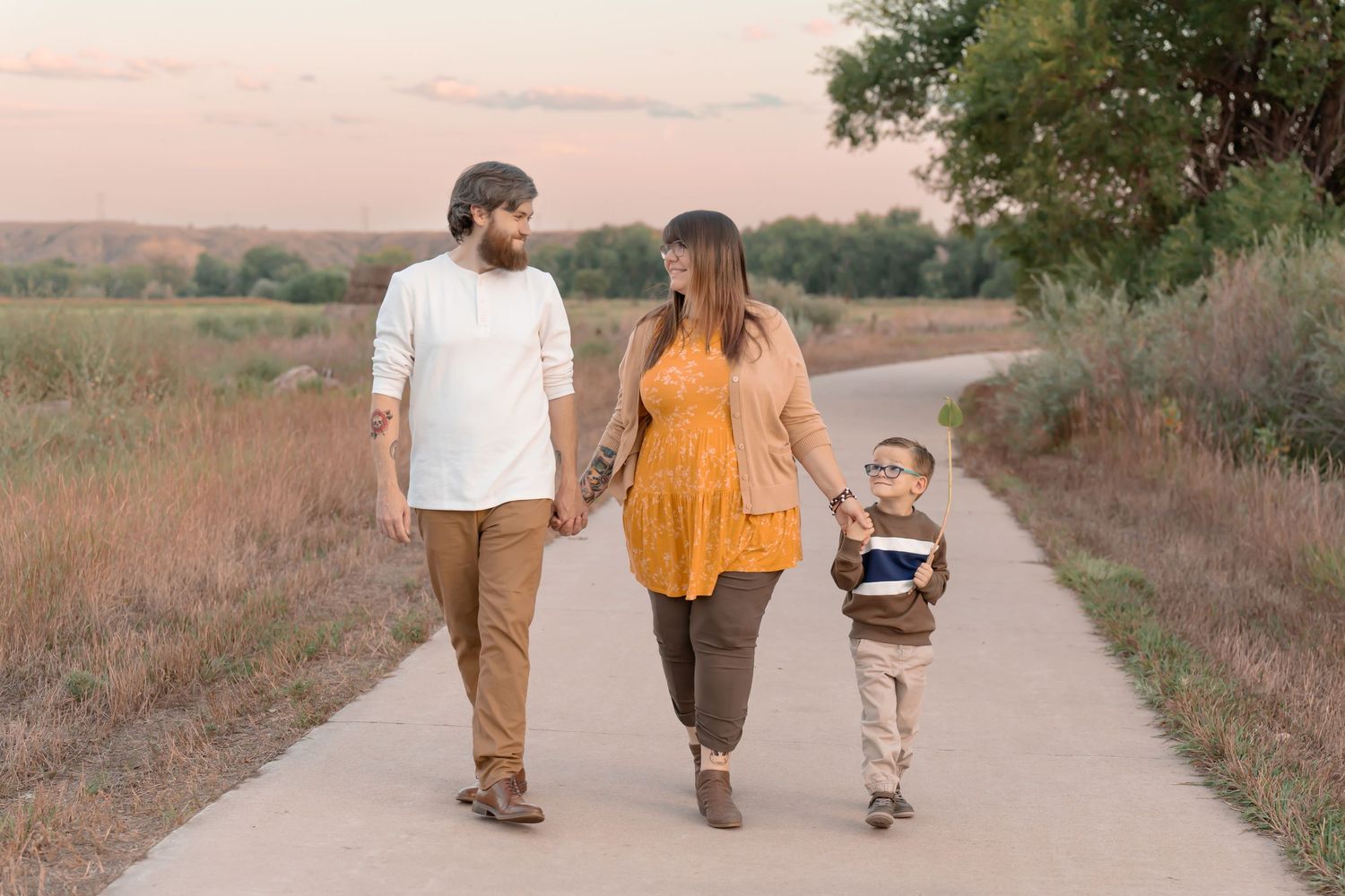 Family walking together down a scenic dirt path with warm autumn colors and natural surroundings.