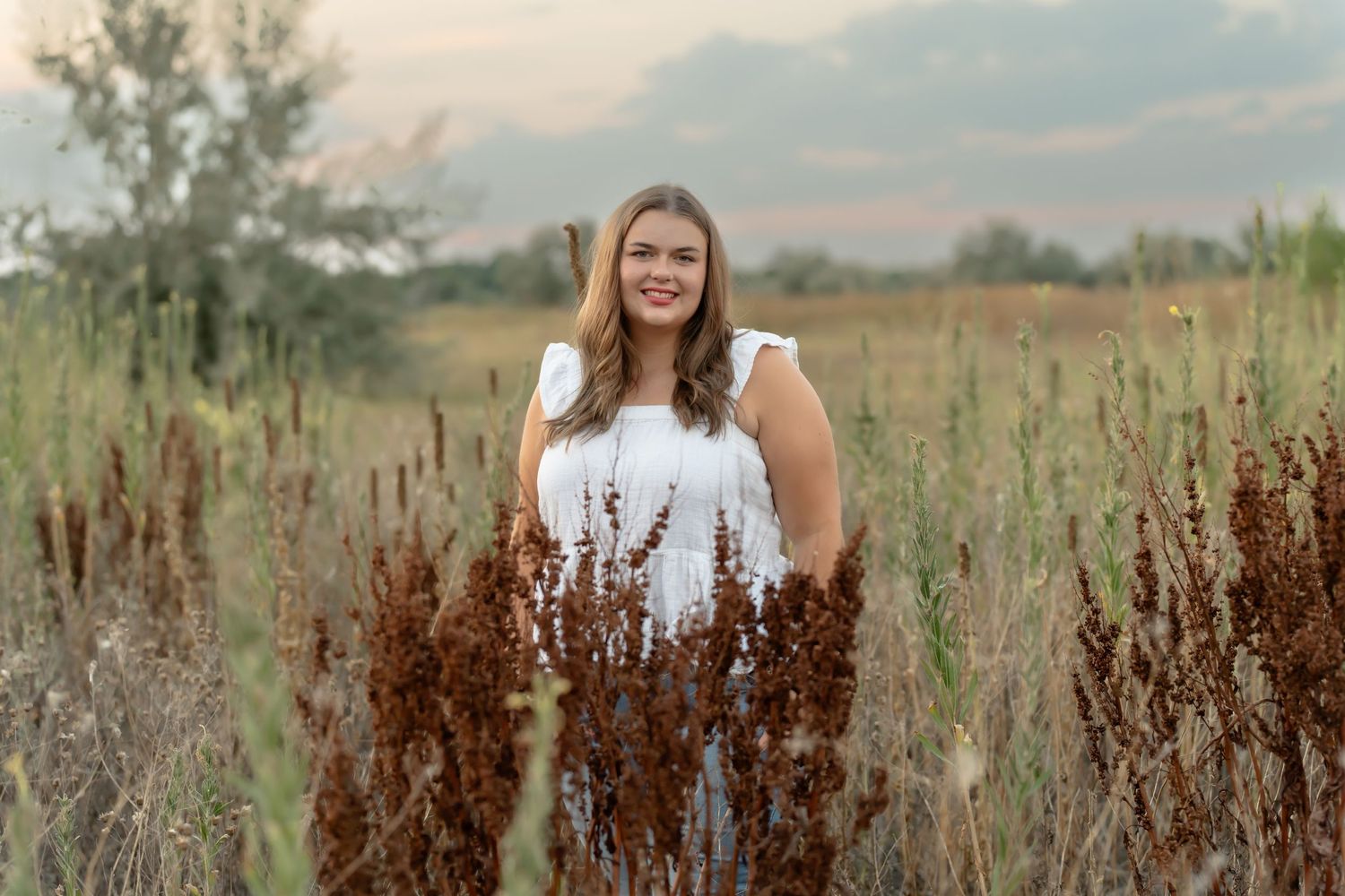 Senior portrait session in a field with dried brown grass during golden hour.