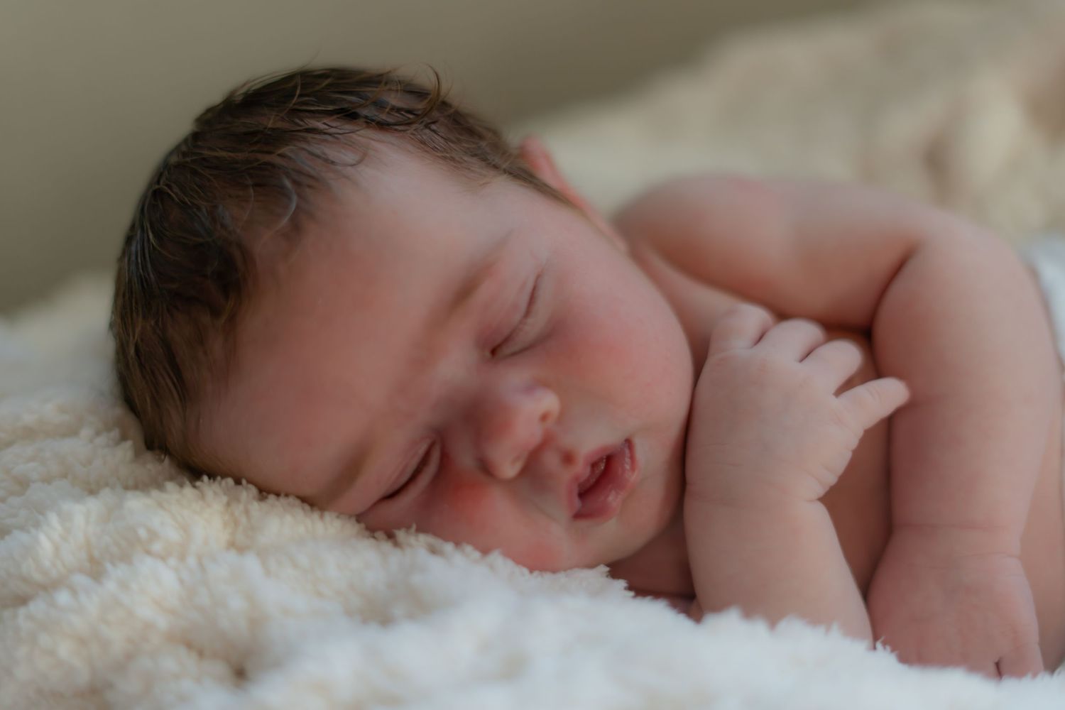 Peaceful sleeping newborn on soft cream blanket.