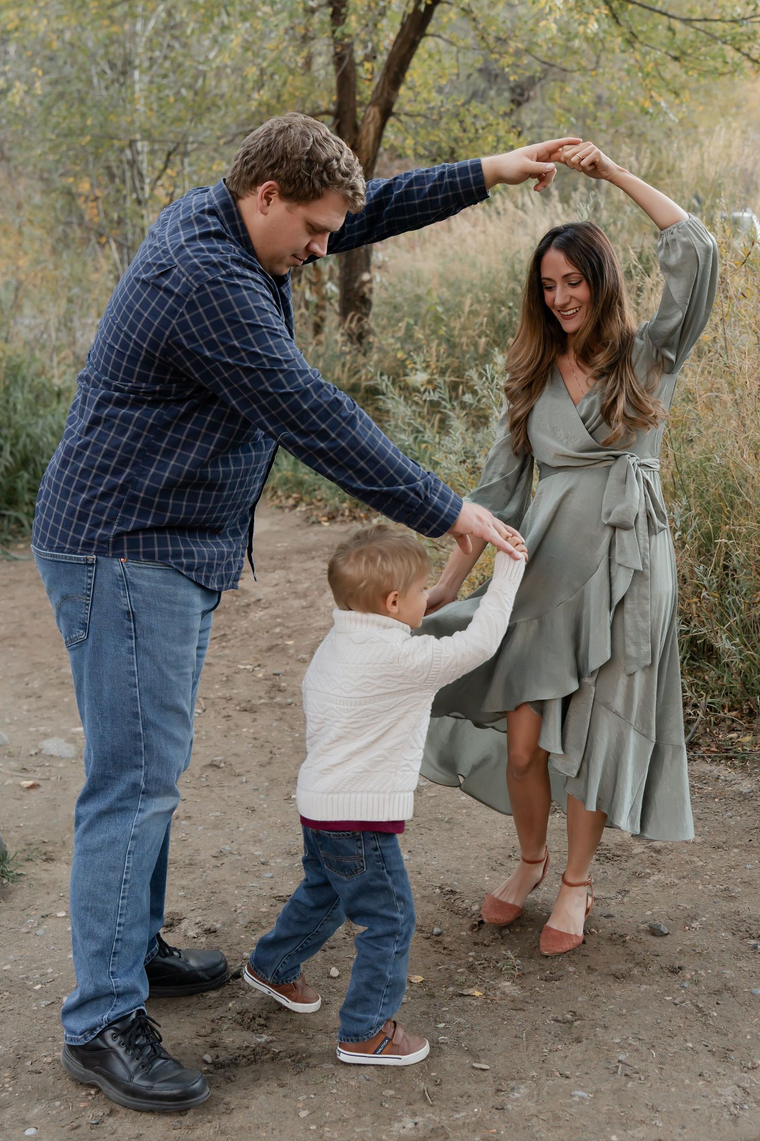 A family dancing together on a dirt trail in casual clothing during an outdoor photoshoot session.