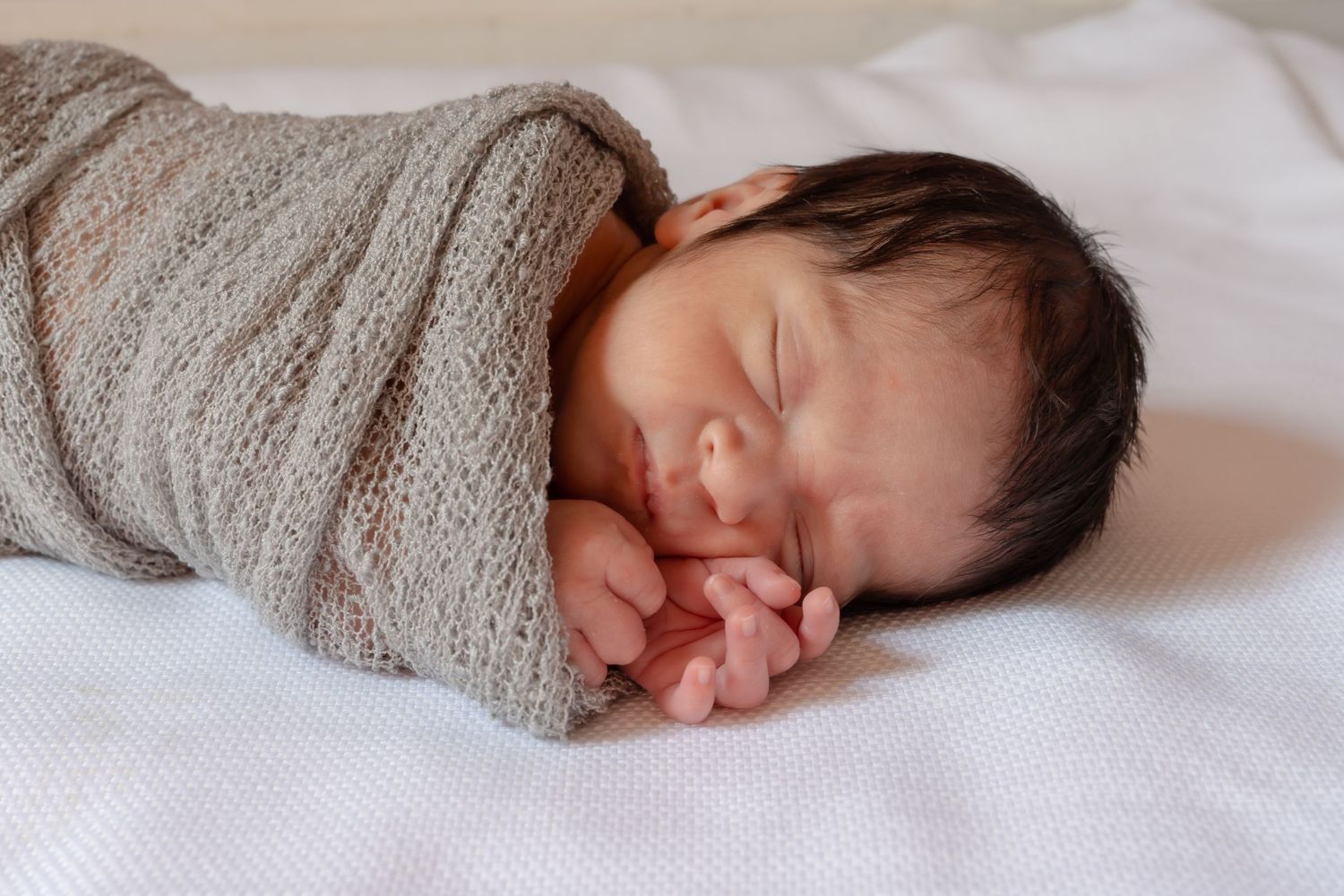 Peaceful sleeping infant nestled in soft gray blankets and white bedding.