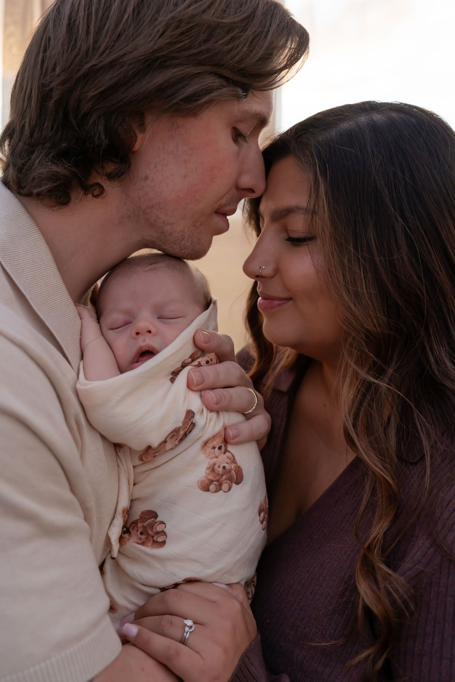 A tender moment between parents and their sleeping baby in a white onesie, shown in multiple progressive shots.