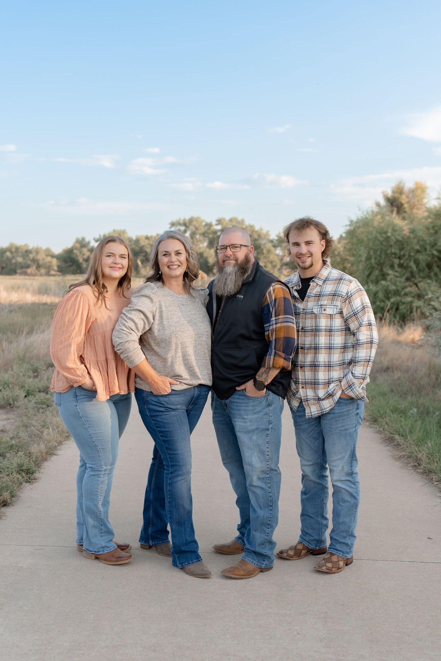 A family of four poses casually on a concrete path wearing coordinated casual outfits in a rural setting.