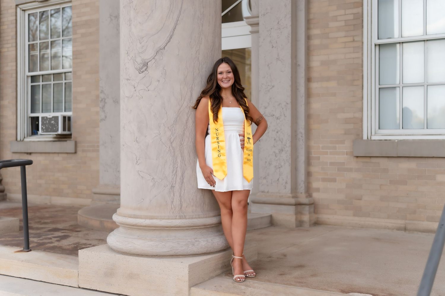 Person in yellow and white dress poses against stone column of building.
