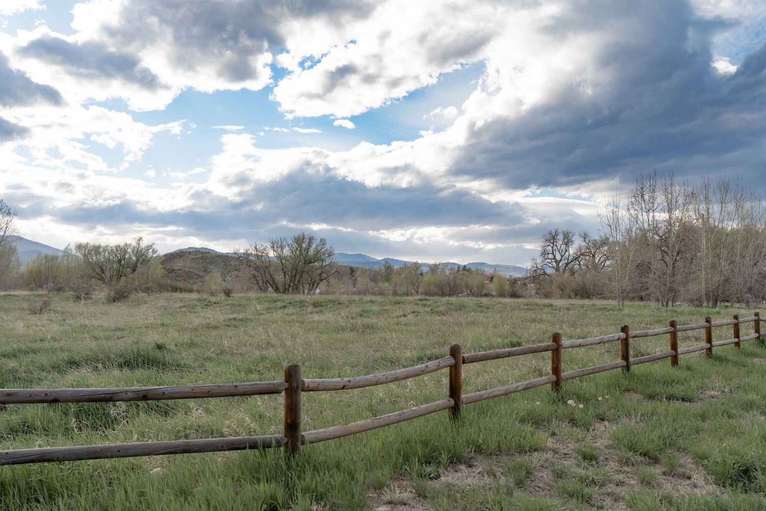 A panoramic view of rolling grasslands with wooden fence posts stretching into the distance under dramatic cloudy skies.