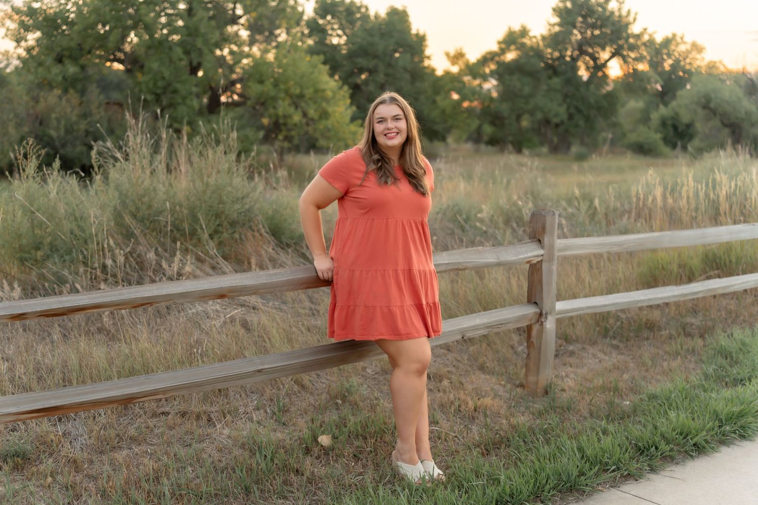Sunset senior portrait session along a rustic wooden fence in golden light.