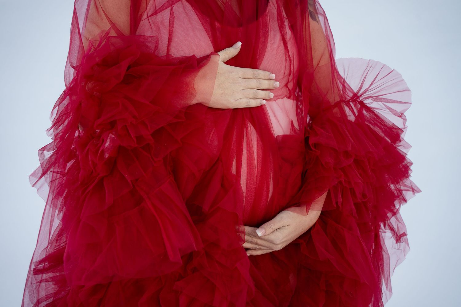 Close-up of flowing red tulle dress fabric with hands cradling belly.