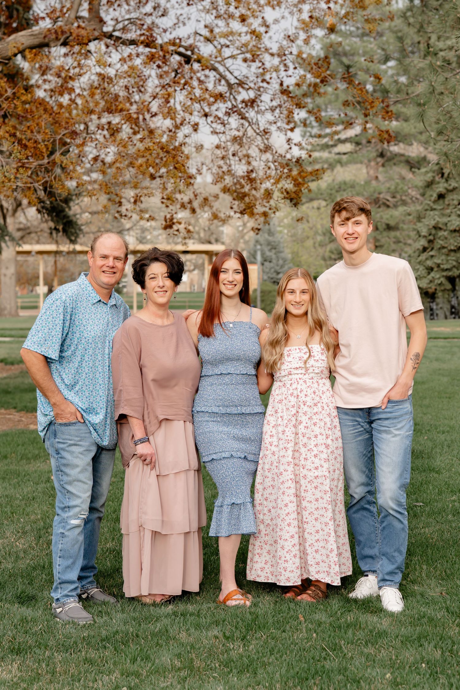 A family of five wearing coordinated pastel outfits poses together on green grass.